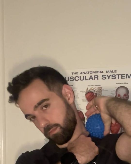 Chris holding a massage ball to his shoulder